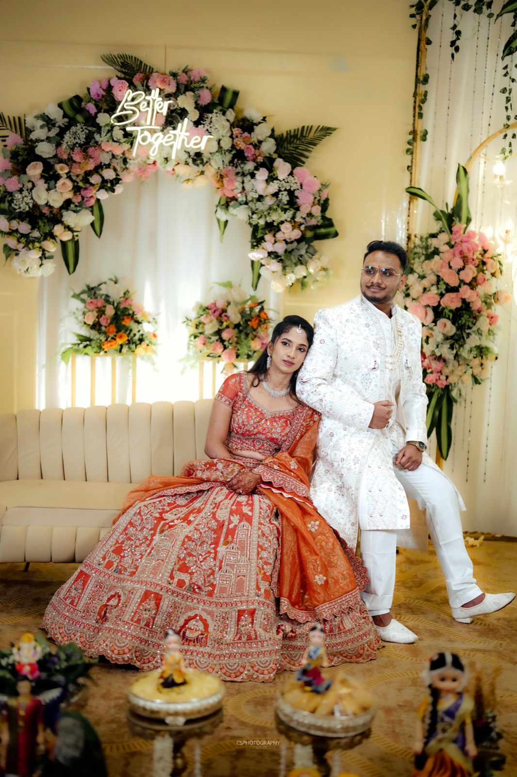 Pooja and Roopak seated under a floral arch